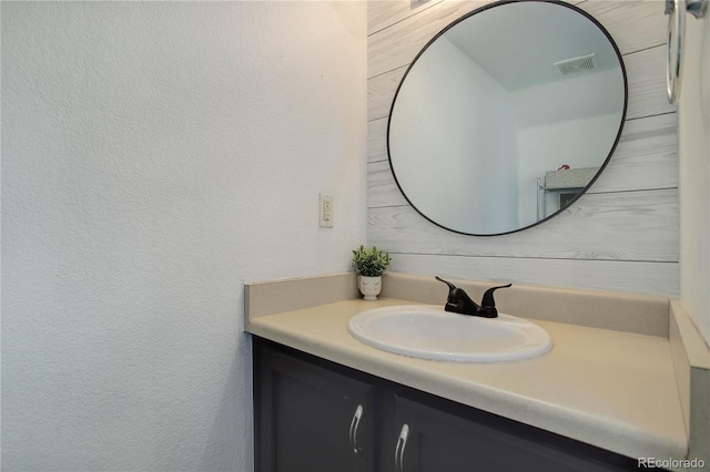 bathroom featuring visible vents, vanity, and a textured wall