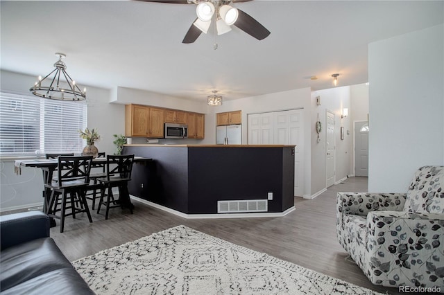 living room with ceiling fan with notable chandelier, light wood-style floors, visible vents, and baseboards