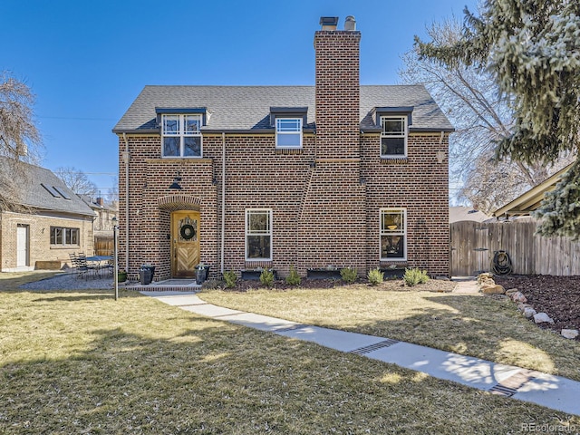 view of front facade featuring brick siding, fence, a front yard, a chimney, and a patio