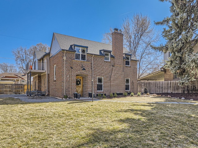 back of house with brick siding, a chimney, a yard, and fence