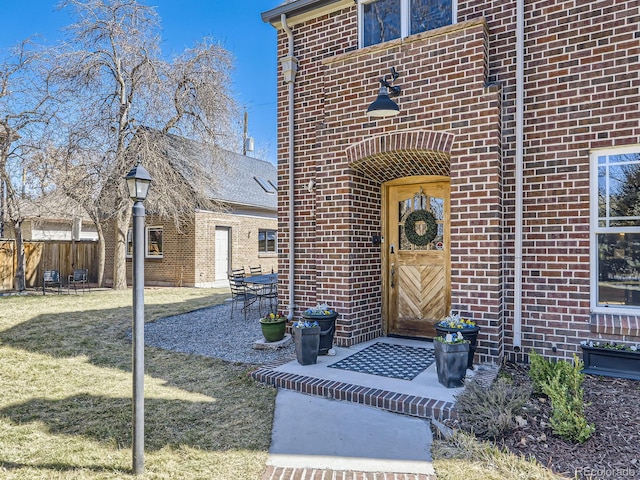 doorway to property with brick siding, a patio area, a lawn, and fence