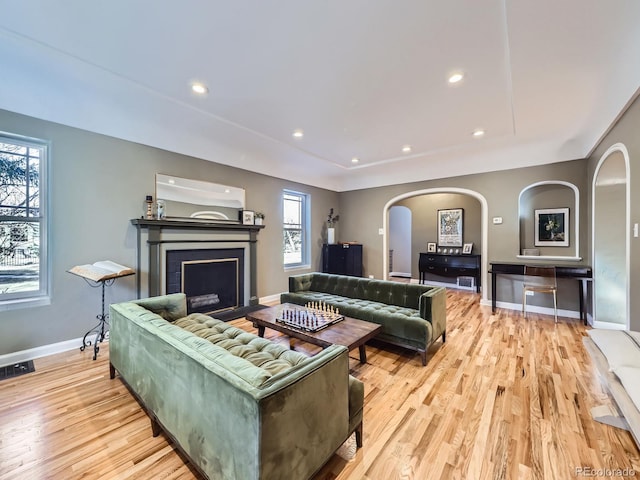 living area with visible vents, a fireplace with flush hearth, light wood-style flooring, arched walkways, and baseboards