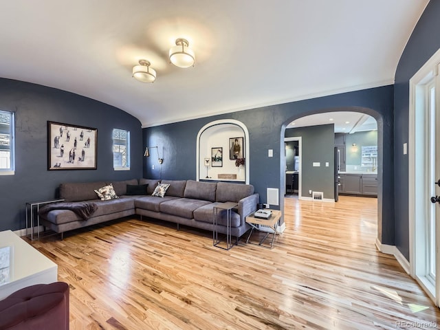 living area featuring lofted ceiling, light wood-style floors, arched walkways, and baseboards