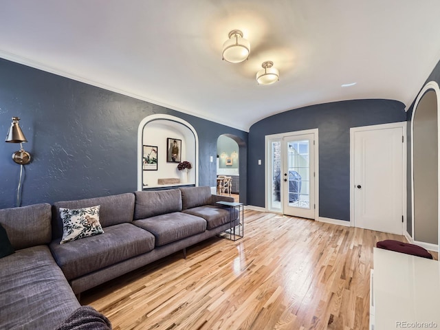 living room with baseboards, light wood-style flooring, arched walkways, vaulted ceiling, and a textured wall