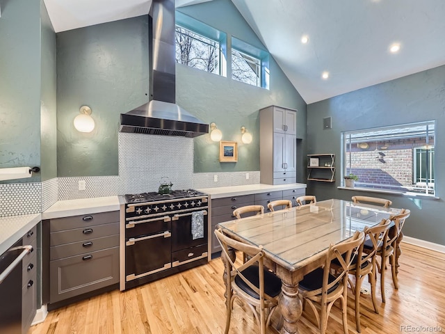 kitchen featuring wall chimney range hood, double oven range, light wood-style floors, and gray cabinetry