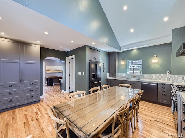 dining area featuring recessed lighting, light wood-style floors, arched walkways, and high vaulted ceiling