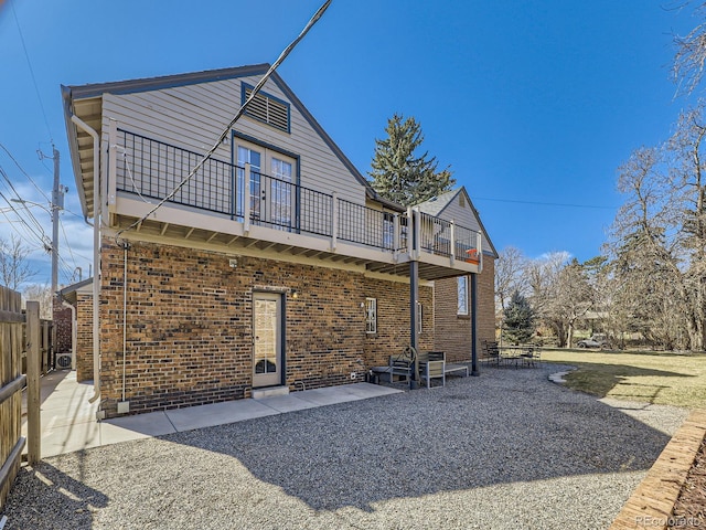 rear view of house with a patio, a balcony, fence, and brick siding