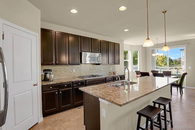 kitchen featuring an island with sink, hanging light fixtures, sink, stainless steel appliances, and a wealth of natural light