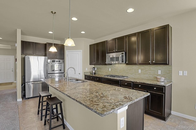 kitchen with appliances with stainless steel finishes, backsplash, decorative light fixtures, a kitchen island with sink, and sink