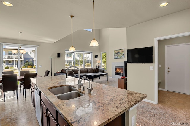 kitchen with an island with sink, light stone countertops, hanging light fixtures, and sink