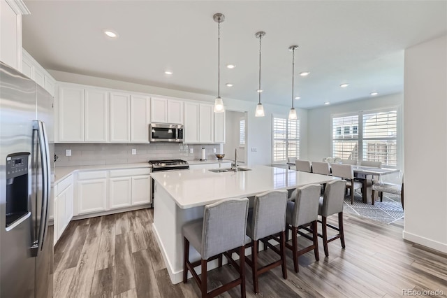 kitchen with appliances with stainless steel finishes, a sink, wood finished floors, white cabinets, and decorative backsplash