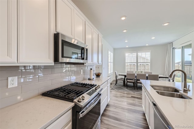kitchen featuring appliances with stainless steel finishes, a sink, white cabinets, backsplash, and light wood-style floors