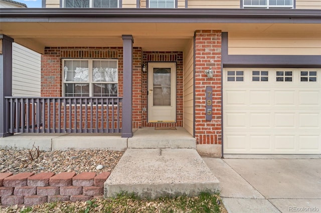 view of exterior entry featuring an attached garage, covered porch, concrete driveway, and brick siding