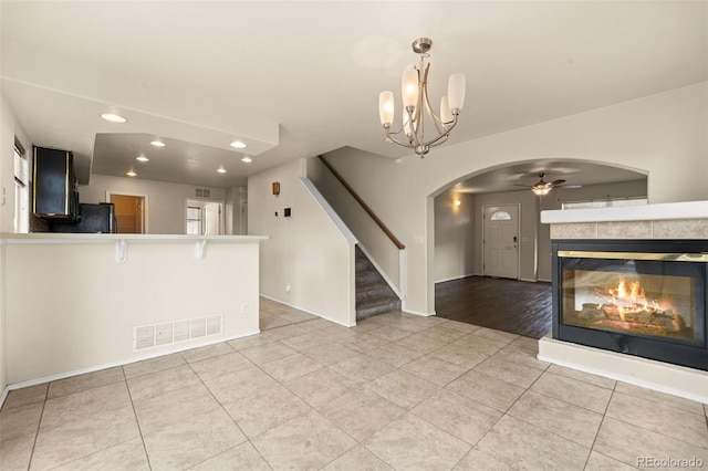unfurnished living room featuring visible vents, light tile patterned floors, arched walkways, stairway, and ceiling fan with notable chandelier