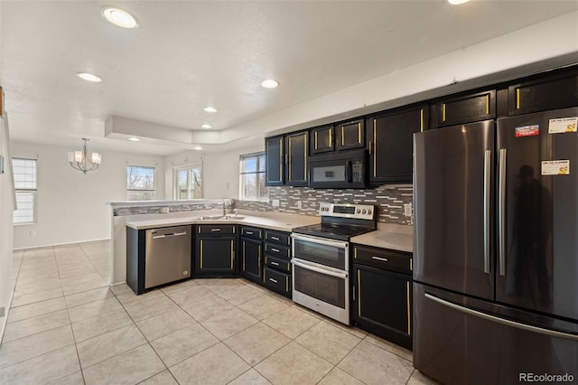kitchen with a peninsula, appliances with stainless steel finishes, light countertops, a sink, and a notable chandelier