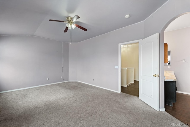interior space featuring ceiling fan, arched walkways, vaulted ceiling, and baseboards