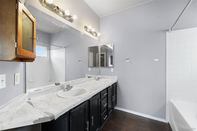 full bathroom featuring wood finished floors, double vanity, a sink, and baseboards