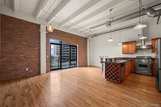 kitchen with stainless steel appliances, hanging light fixtures, kitchen peninsula, brick wall, and a high ceiling