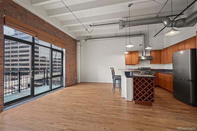 kitchen featuring brick wall, appliances with stainless steel finishes, decorative light fixtures, a kitchen bar, and a high ceiling