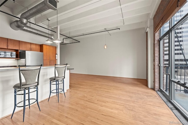 kitchen featuring decorative light fixtures, stainless steel appliances, a breakfast bar, and light wood-type flooring