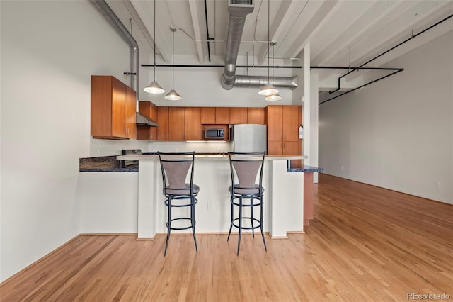 kitchen featuring light hardwood / wood-style flooring, appliances with stainless steel finishes, a towering ceiling, a kitchen breakfast bar, and decorative light fixtures