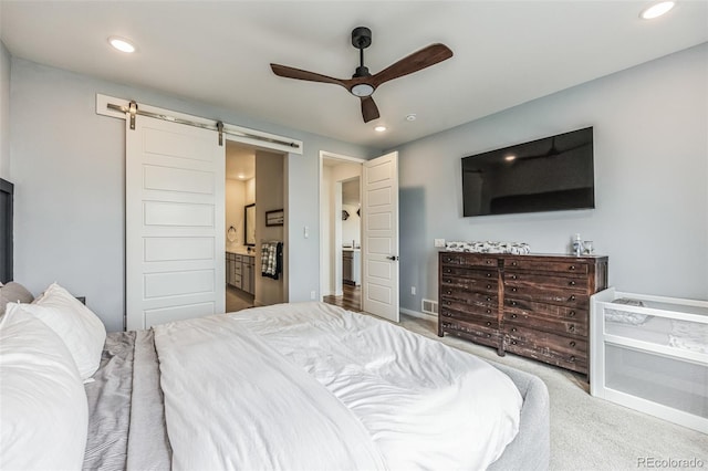 carpeted bedroom with a barn door, ceiling fan, and ensuite bathroom