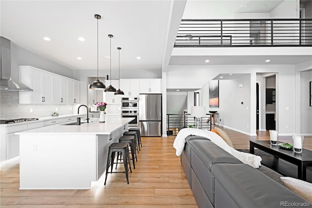 kitchen with wall chimney range hood, sink, decorative light fixtures, appliances with stainless steel finishes, and a large island