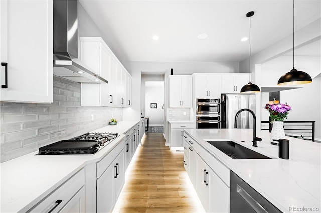 kitchen featuring white cabinetry, sink, hanging light fixtures, stainless steel appliances, and wall chimney range hood