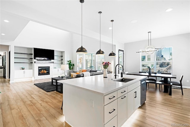 kitchen featuring built in shelves, sink, pendant lighting, a center island with sink, and white cabinets