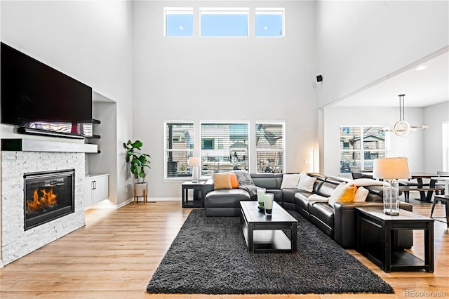 living room featuring a chandelier, a fireplace, a high ceiling, and light hardwood / wood-style flooring