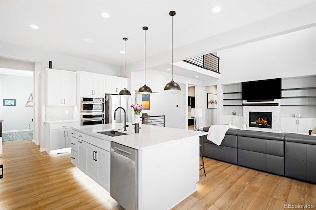 kitchen with hanging light fixtures, stainless steel appliances, an island with sink, light hardwood / wood-style floors, and white cabinets