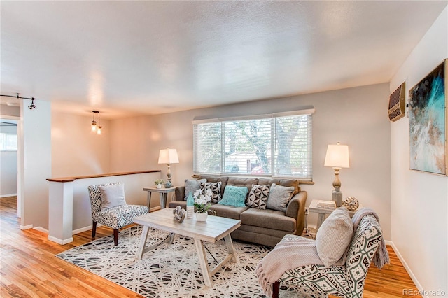 living room featuring light wood-style flooring, baseboards, and a wall mounted AC