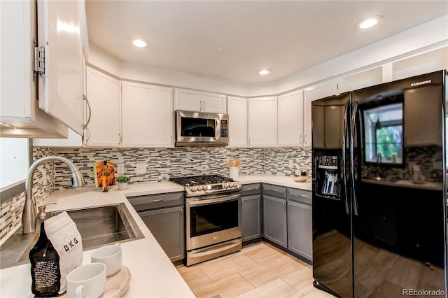 kitchen featuring appliances with stainless steel finishes, a sink, gray cabinets, light countertops, and white cabinetry
