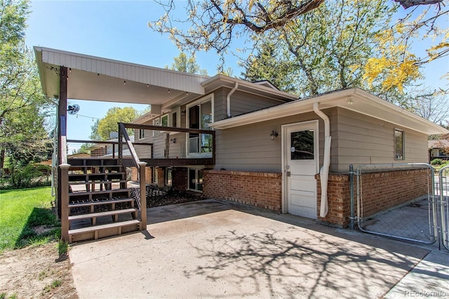 view of property exterior featuring brick siding, stairway, a gate, a wooden deck, and a patio