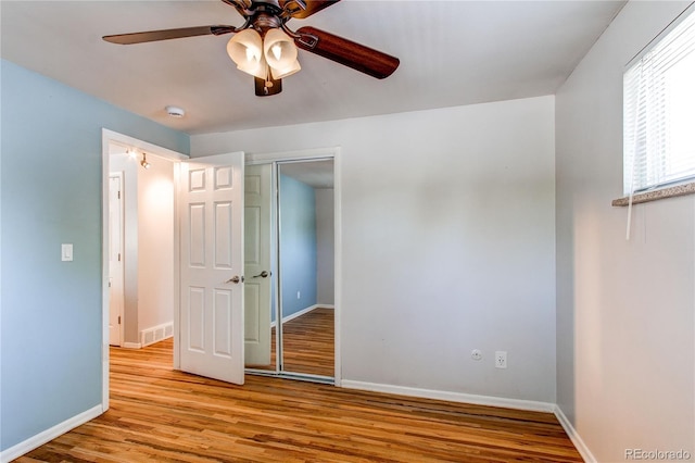unfurnished bedroom with wood finished floors, a closet, baseboards, and a ceiling fan