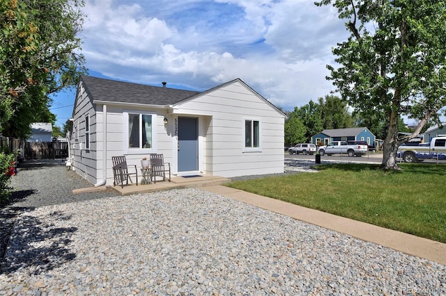 bungalow featuring a front lawn, roof with shingles, and fence