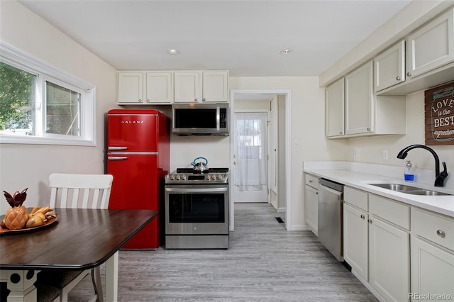 kitchen featuring stainless steel appliances, light countertops, a sink, and white cabinetry