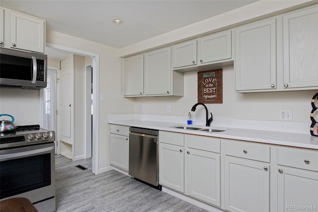 kitchen featuring light wood finished floors, light countertops, appliances with stainless steel finishes, white cabinets, and a sink