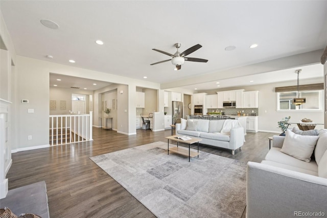 living room featuring ceiling fan, dark wood-type flooring, and a healthy amount of sunlight