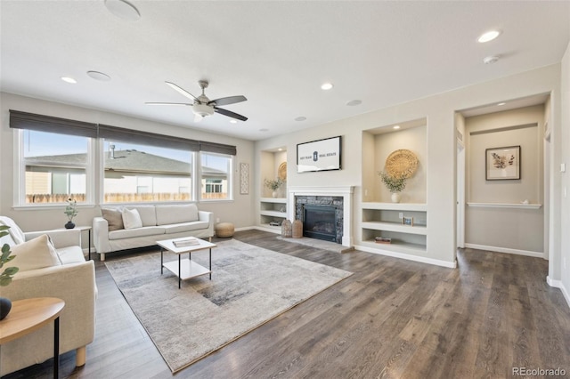 living room with dark wood-type flooring, ceiling fan, a fireplace, and built in shelves