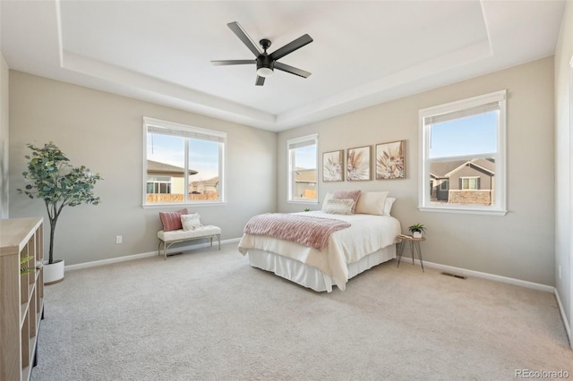 bedroom with a raised ceiling, light colored carpet, and ceiling fan