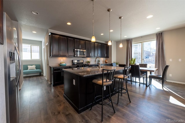 kitchen featuring sink, a kitchen island with sink, hanging light fixtures, stainless steel appliances, and dark hardwood / wood-style flooring