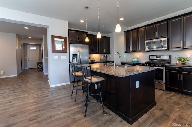 kitchen with appliances with stainless steel finishes, stone countertops, a kitchen island with sink, and hanging light fixtures