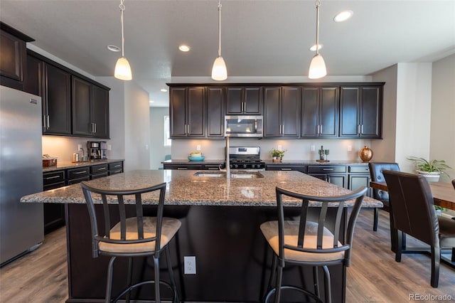 kitchen with pendant lighting, dark brown cabinetry, stainless steel appliances, and a center island with sink