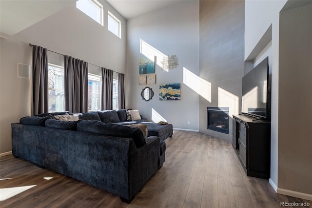 living room with a towering ceiling, dark hardwood / wood-style flooring, and a tile fireplace