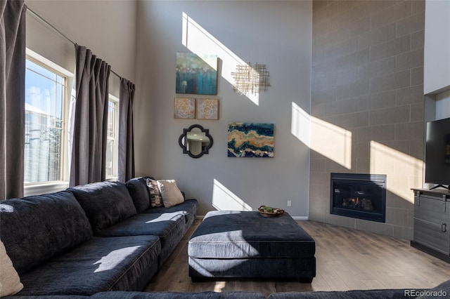 living room with a tiled fireplace, wood-type flooring, and a towering ceiling