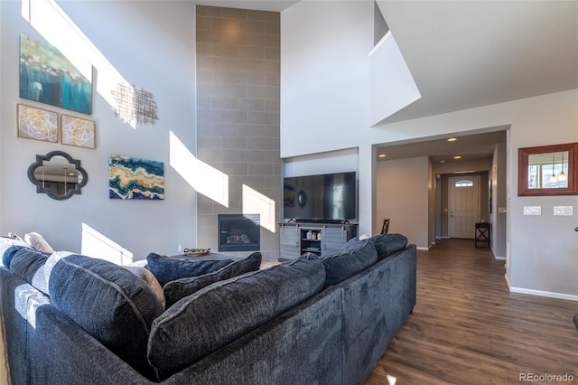 living room with dark hardwood / wood-style floors, a tiled fireplace, and a high ceiling