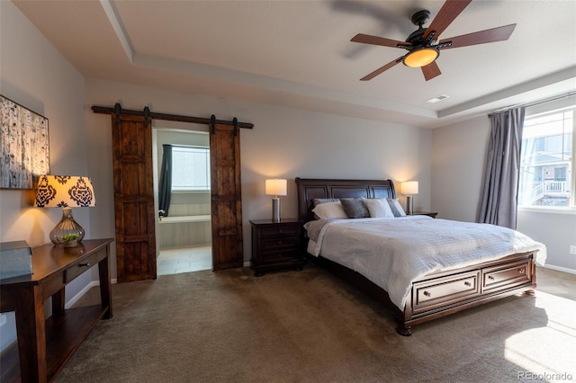 bedroom featuring ensuite bath, a barn door, a raised ceiling, and dark colored carpet