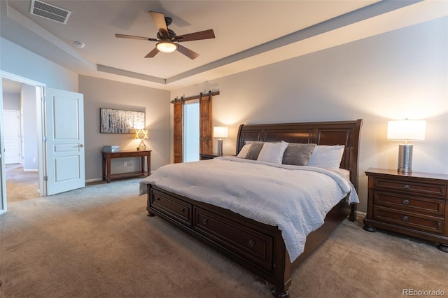 carpeted bedroom featuring a barn door, ceiling fan, and a tray ceiling