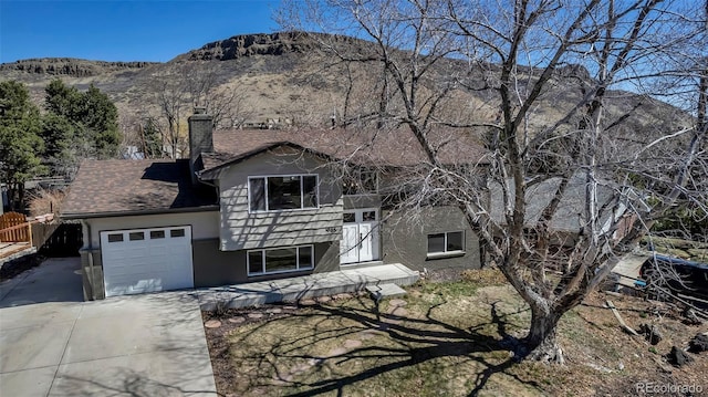 view of front of house featuring driveway, stucco siding, a chimney, a garage, and a mountain view